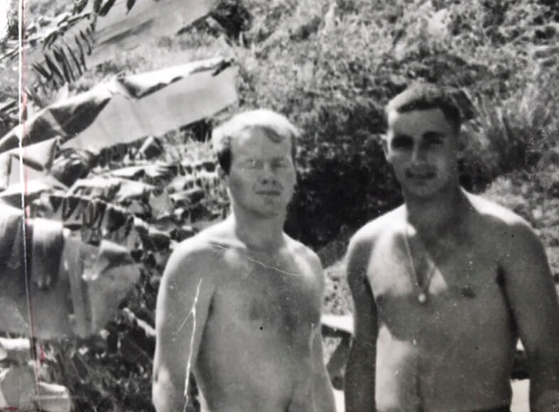 Black and white photo of two shirtless Vietnam War soldiers in the jungle.