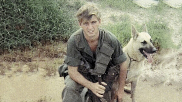 A young soldier crouching down with his German Shepherd scout dog.