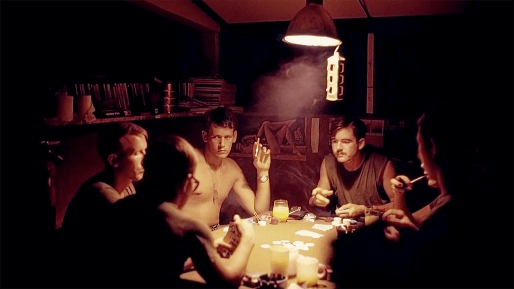 5 men in a dimly lit hooch smoking cigarettes and playing poker.