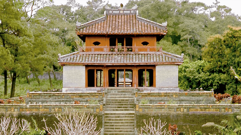 Exterior of a simple two-storied Asian temple, surrounded by greenery and gardens.