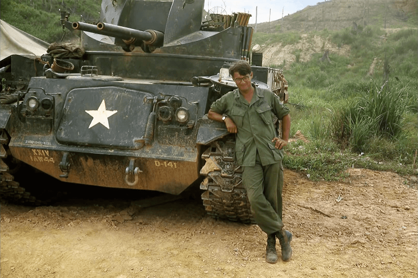 A soldier leaning against a tank with a white star painted on its front.