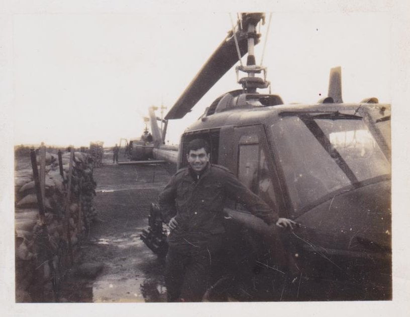 A young soldier leaning against a helicopter.