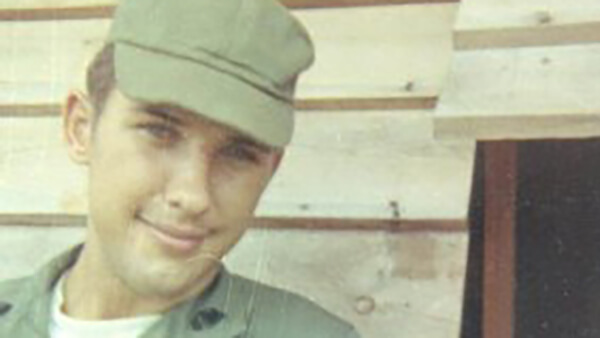 A young soldier with a green cap and slight smile on his face.