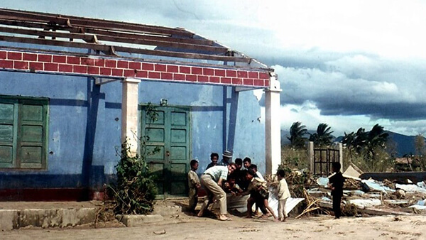 A US civilian crouching down with Asian children outside of a blue single-story building.