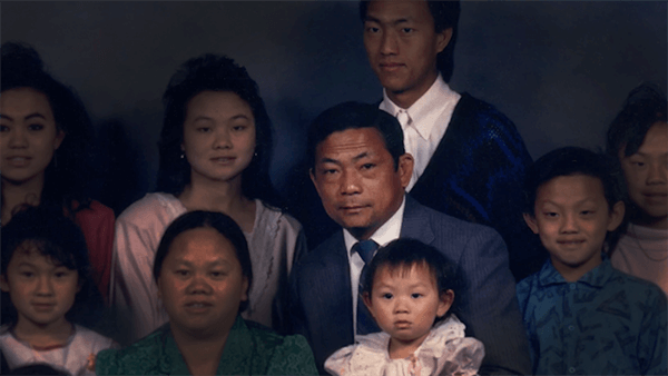 Professional portrait of a large Hmong family. The patriarch is well lit and the other family members are more dimly lit.