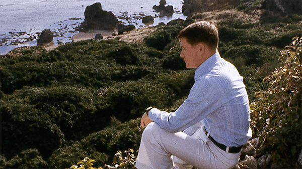 A young man in civilian clothes sitting and peering out onto a body of water.