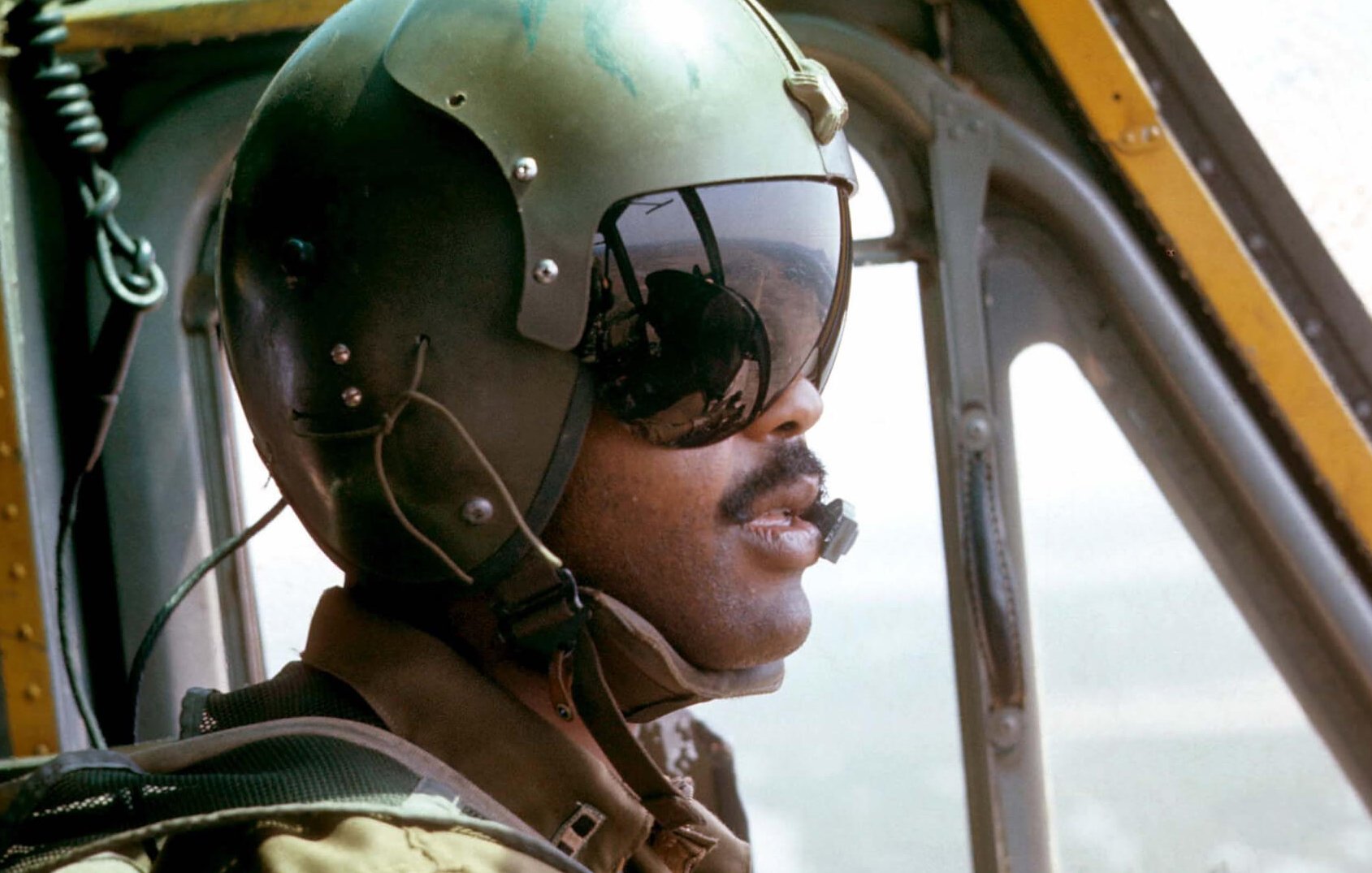 African American pilot in a helicopter wearing a green helmet.