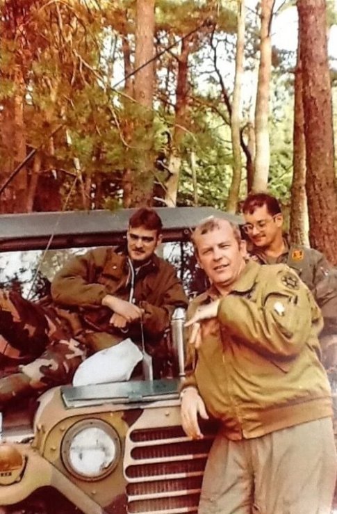 Three US soldiers posing with a Jeep in a forest.