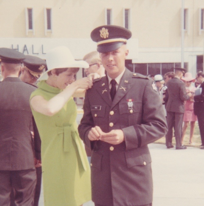 Woman in a green dress pinning military bars on a soldier's uniform.