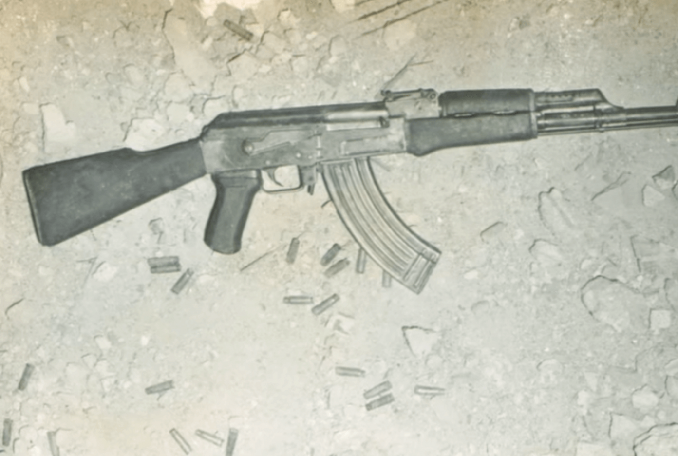 A rifle and shells laying on a dusty ground.
