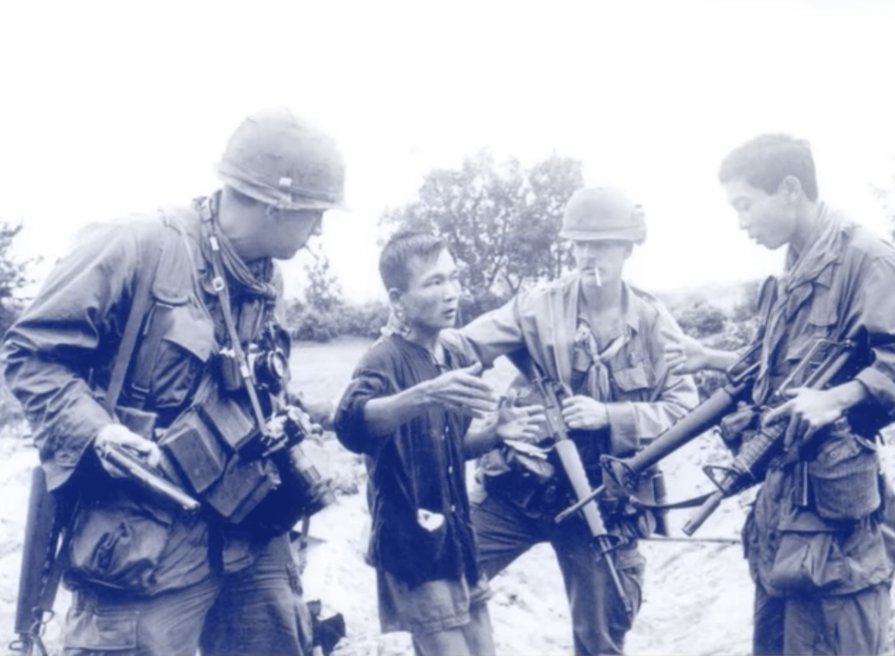 Two US soldiers holding an Asian soldier captive, talking to an allied Asian soldier.