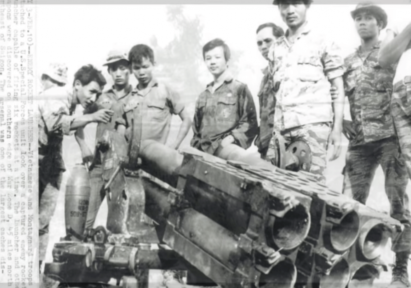 A group of Asian soldiers standing around and looking at a large piece of weaponry.