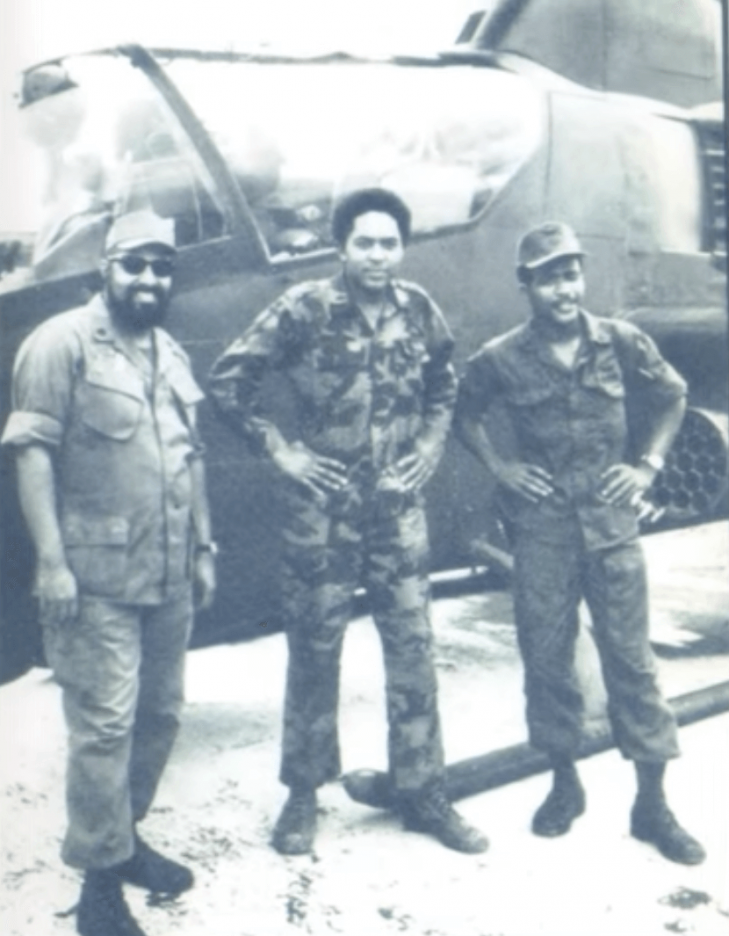 Three African American soldiers posing in front of a helicopter.
