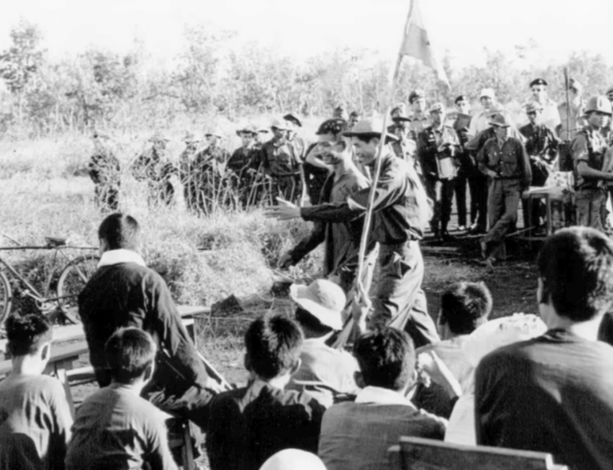 A group of Asian soldiers gathered around as two soldiers walk through the center of the crowd.