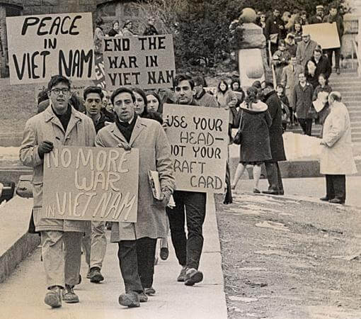 Students walking, carrying signs that say, "Peace in Viet Nam," "End the war in Viet Nam," No more war in Vietnam," and "use your head -- not your draft card."