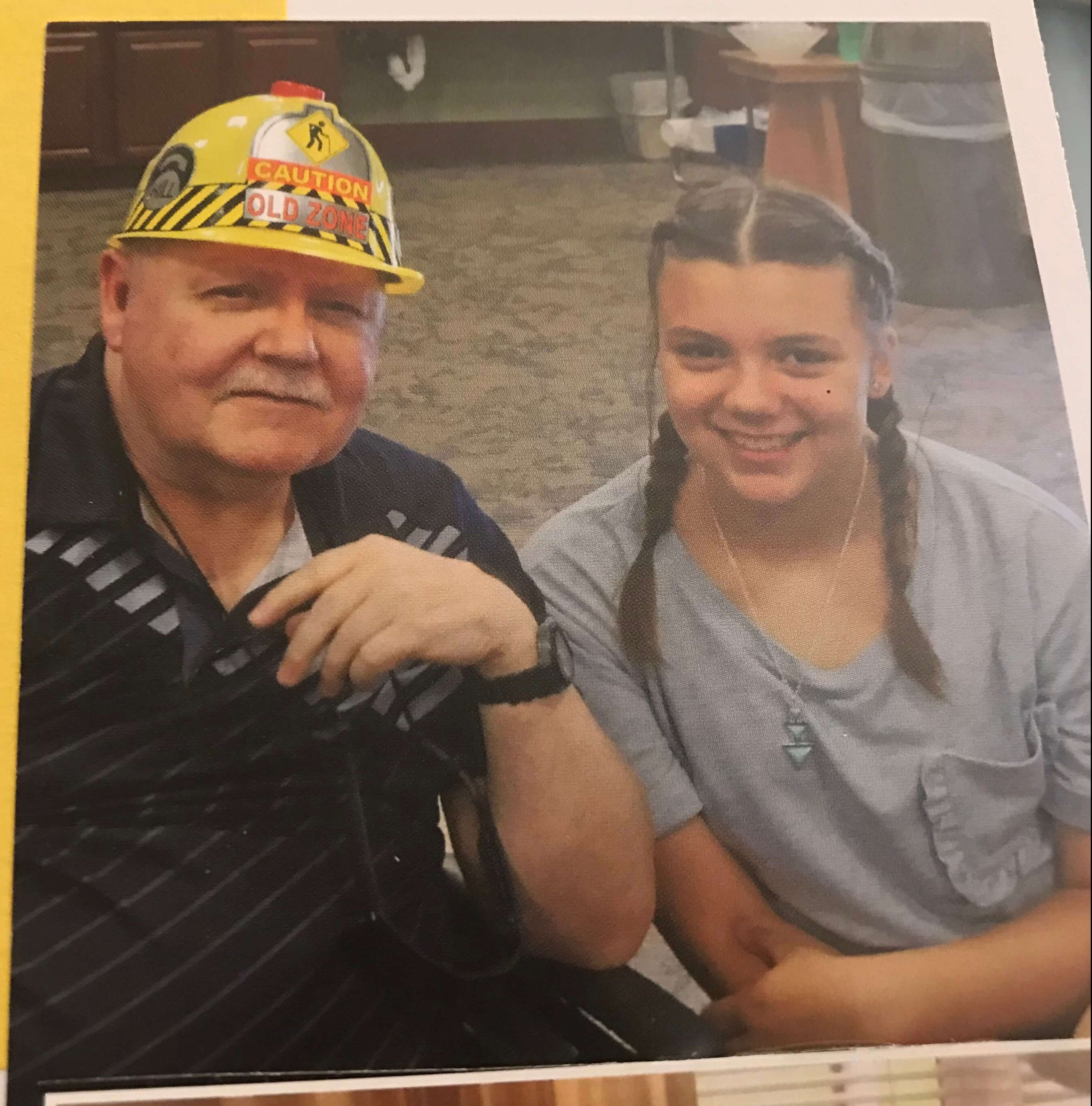 Photo of a scrapbook page that includes an older gentleman in a toy hard hat that says "Caution Old Zone" and a young girl in pigtails.