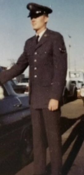 A young man in a navy blue uniform, standing next to a car.