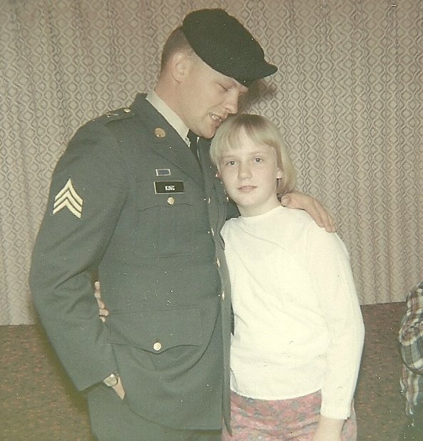 A US soldier in uniform and green beret, hugging his little sister.