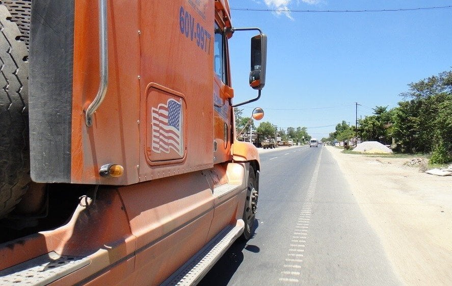 Modern day photo of an orange semi truck along a highway.