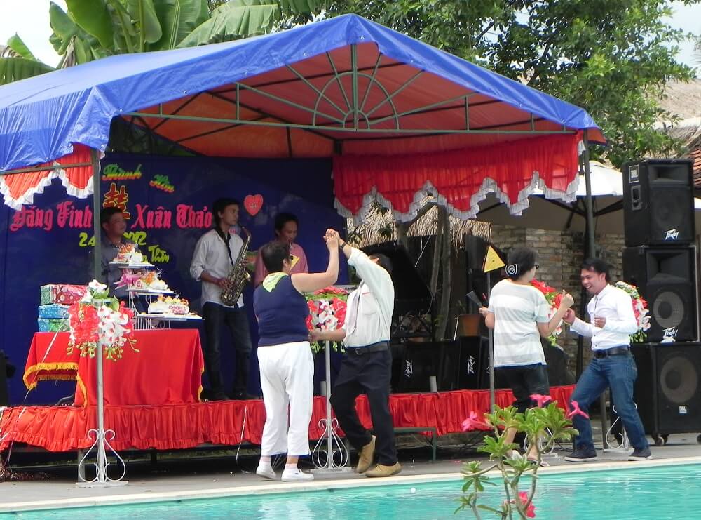 Contemporary photo of Asian people dancing poolside while a band plays under a tented stage.