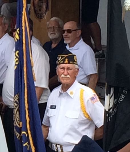 Older male veteran in uniform with flags.