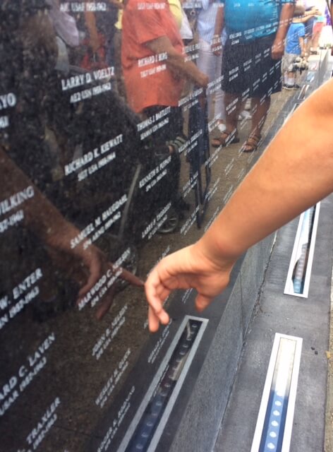 Finger pointing to names on a black memorial.