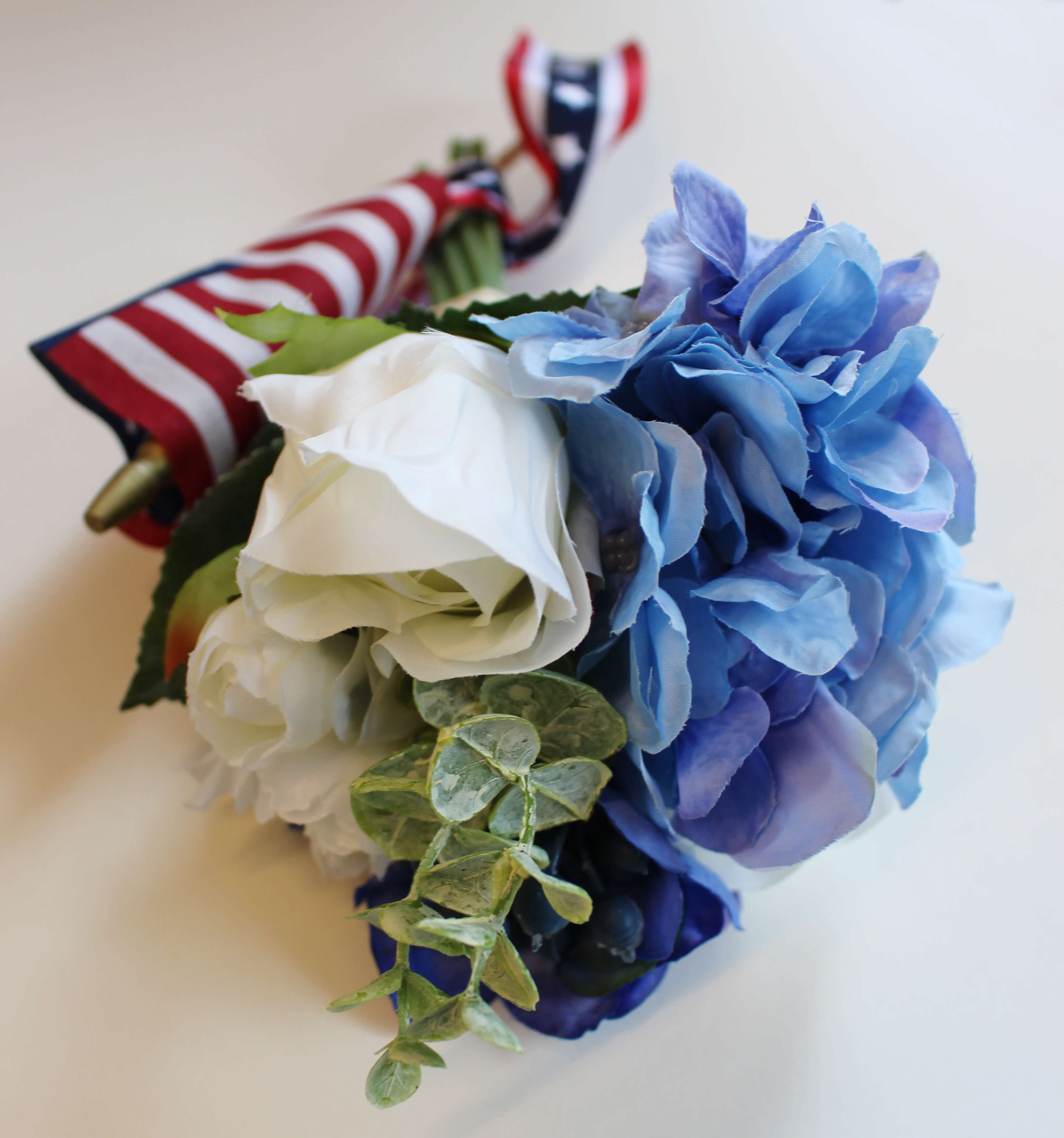 White and blue flowers in a bouquet with an American flag and ribbon