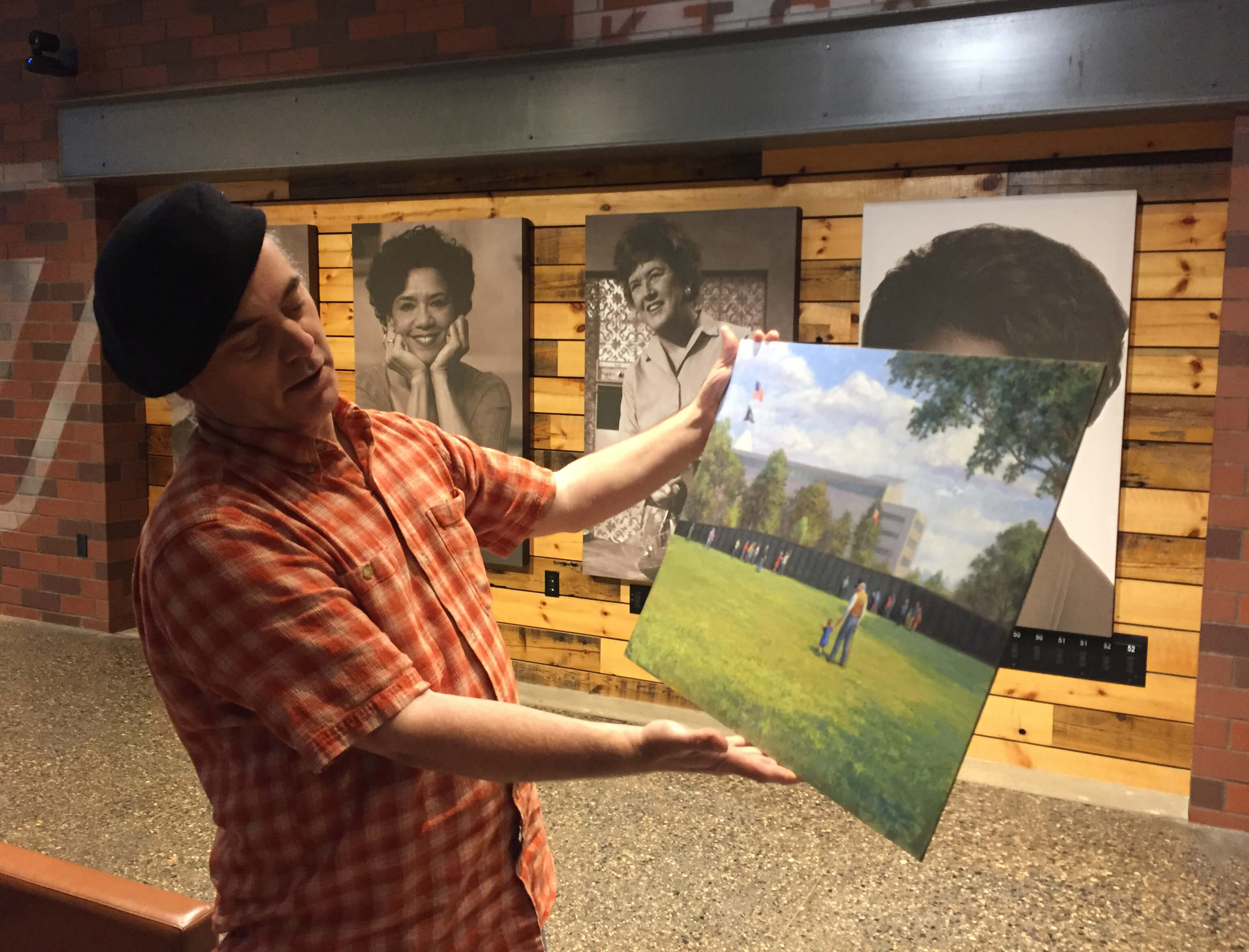 Man holding an oil painting of a landcscape and replica of the Vietnam Wall.