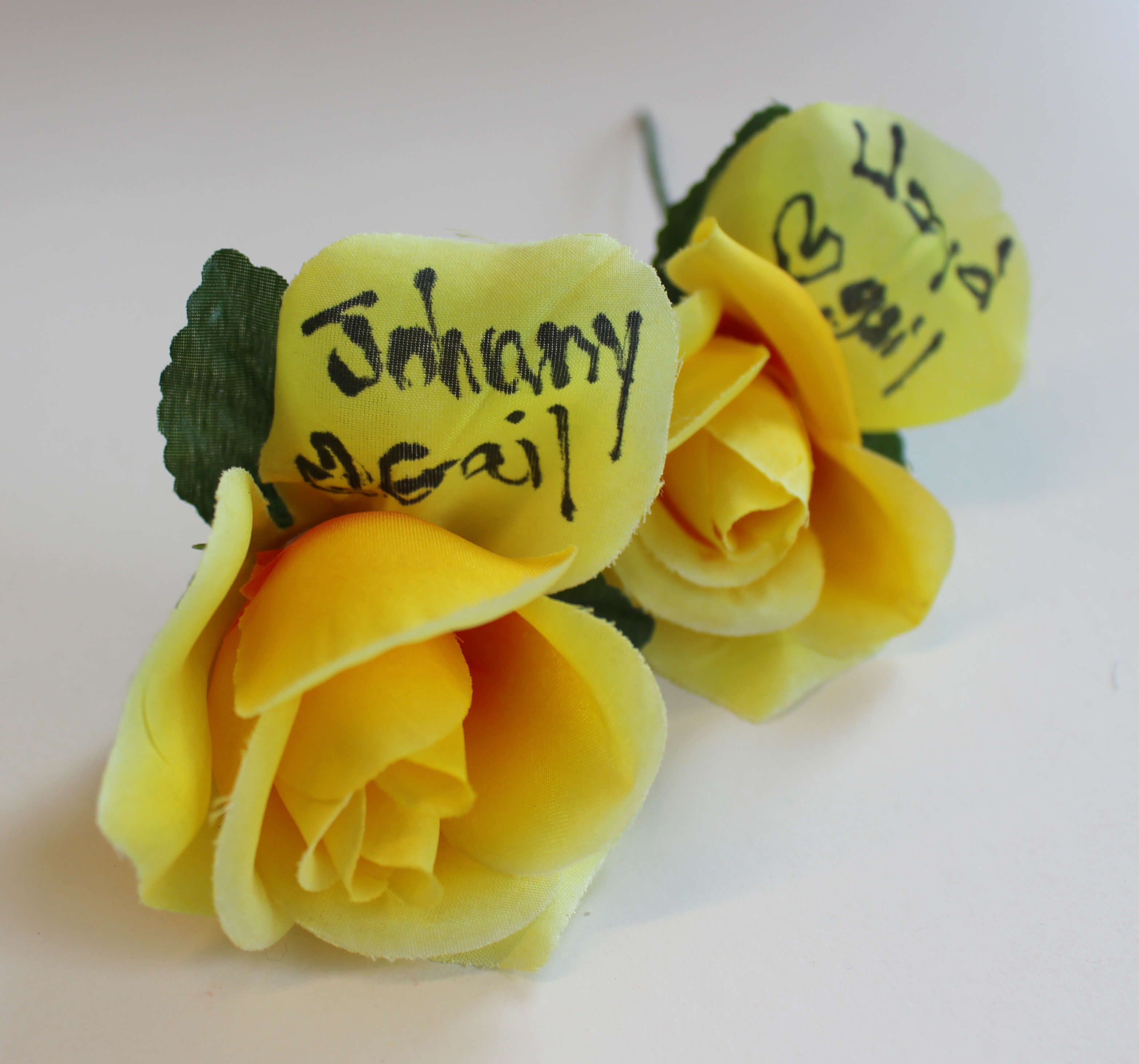 Two fake yellow roses with notes written on them.