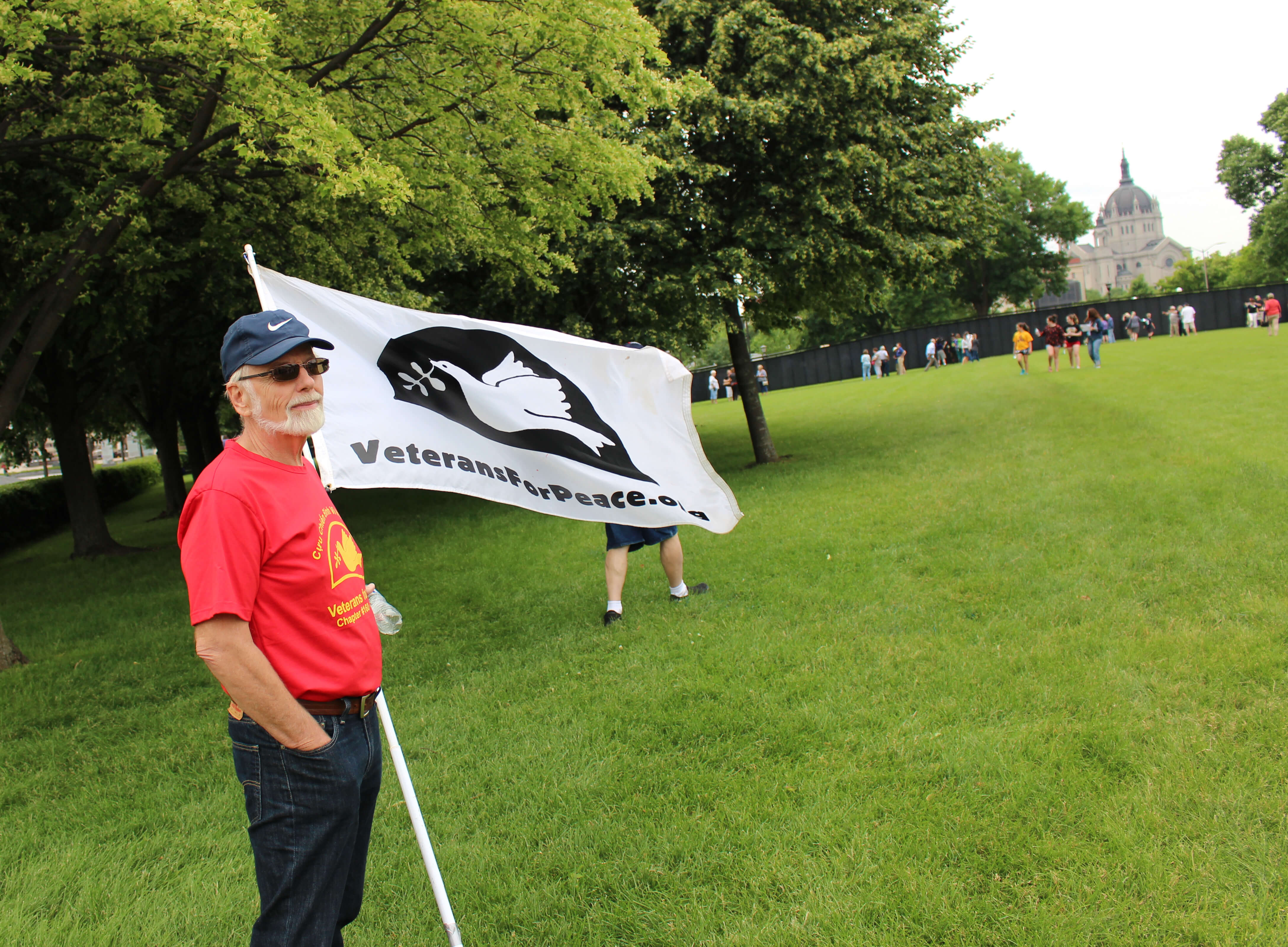 Man in red shirt holding a Veterans for Peace flag.