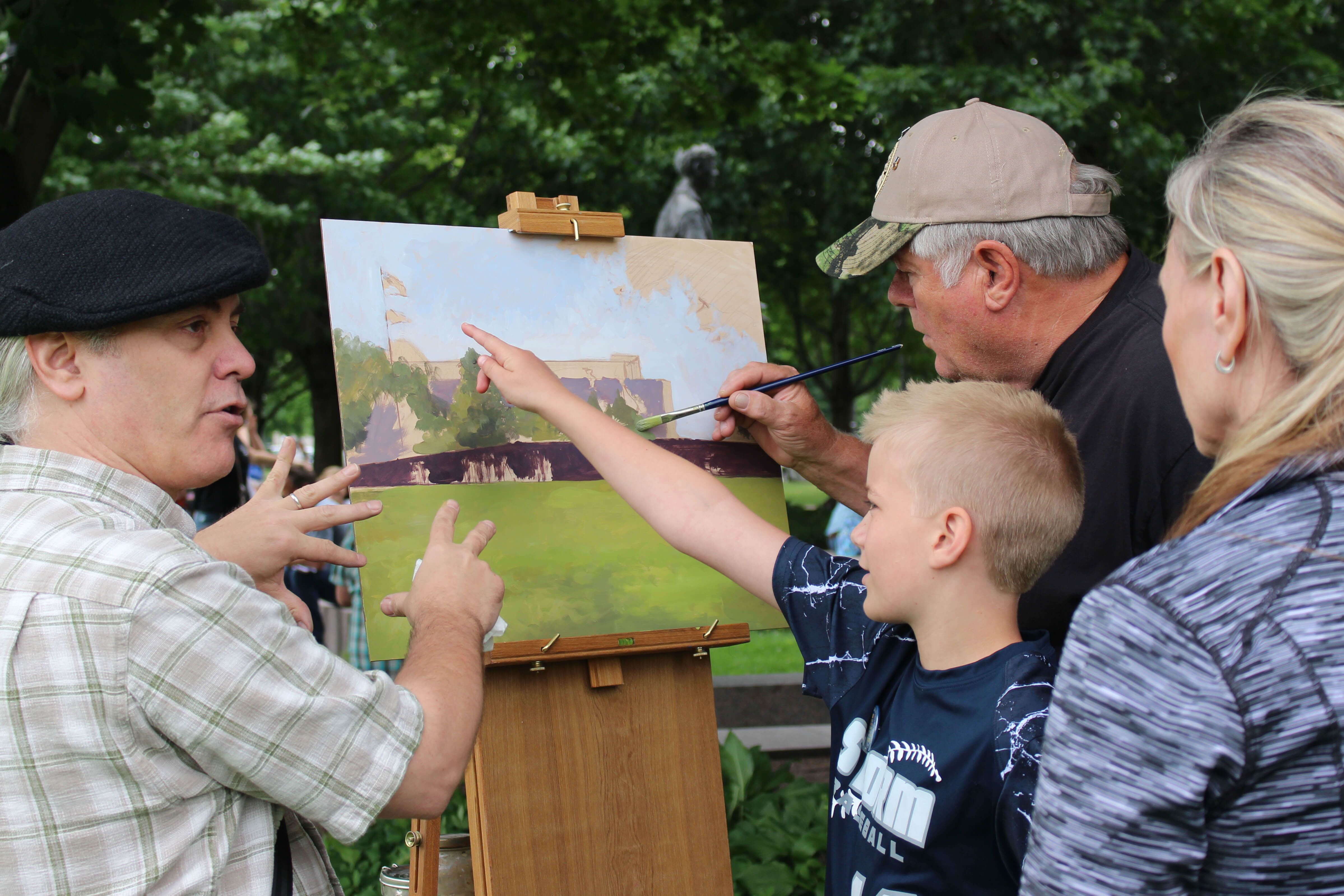 Group of people painting on a canvas outside.
