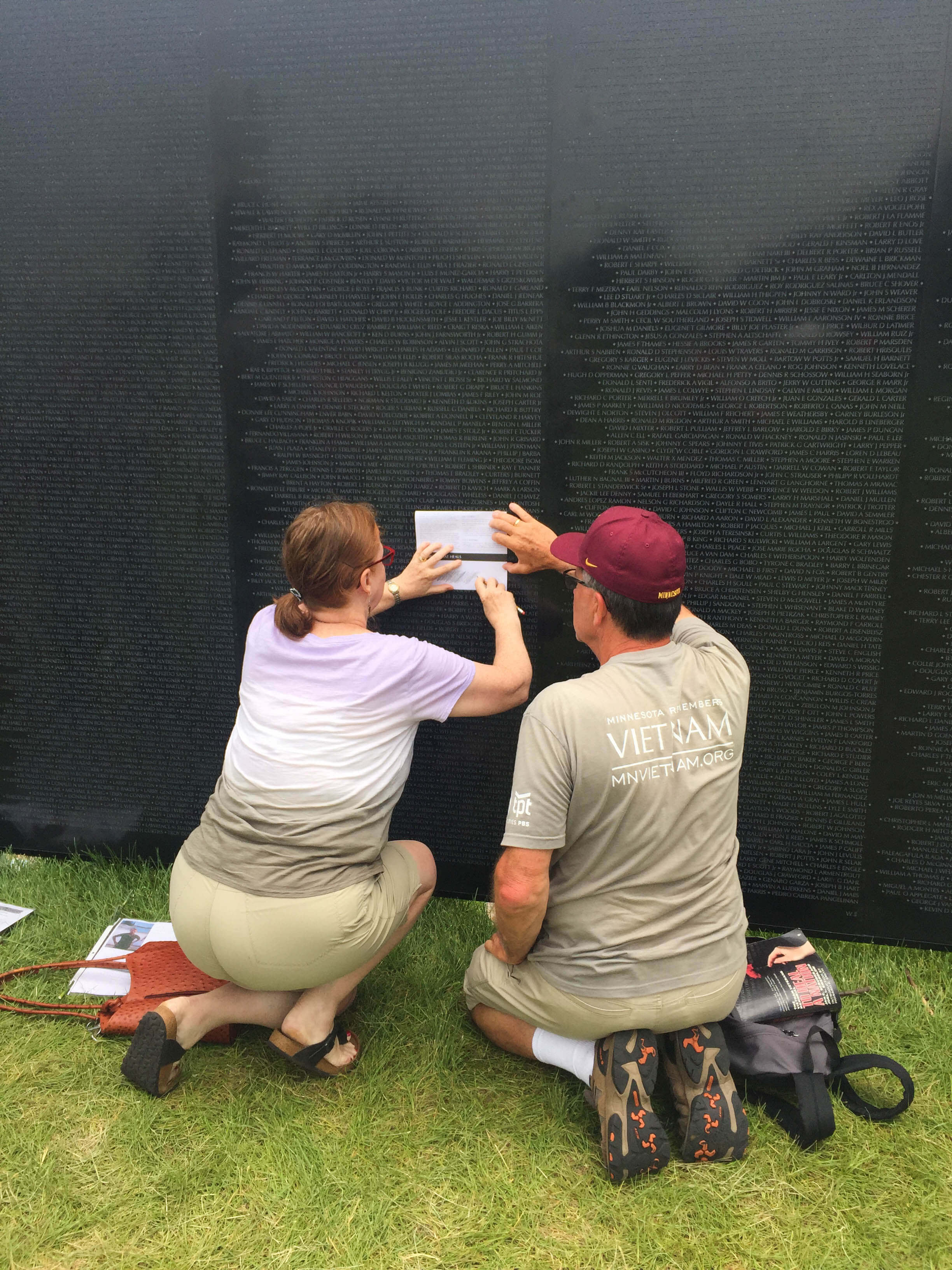 Man helping a woman do a name rubbing at a replica of the Vietnam Wall.
