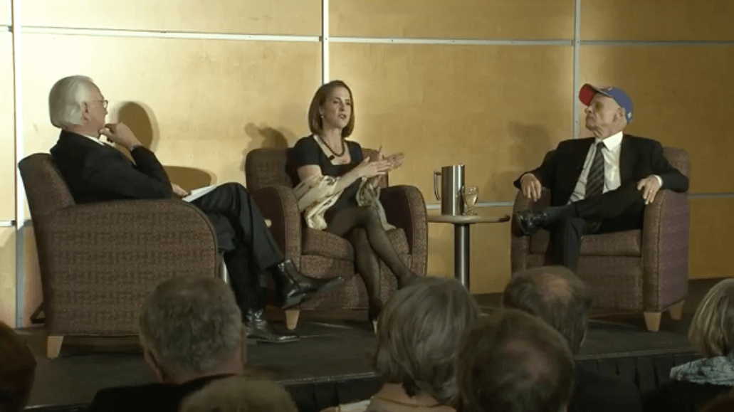 Three people sitting in chairs on stage at en event.