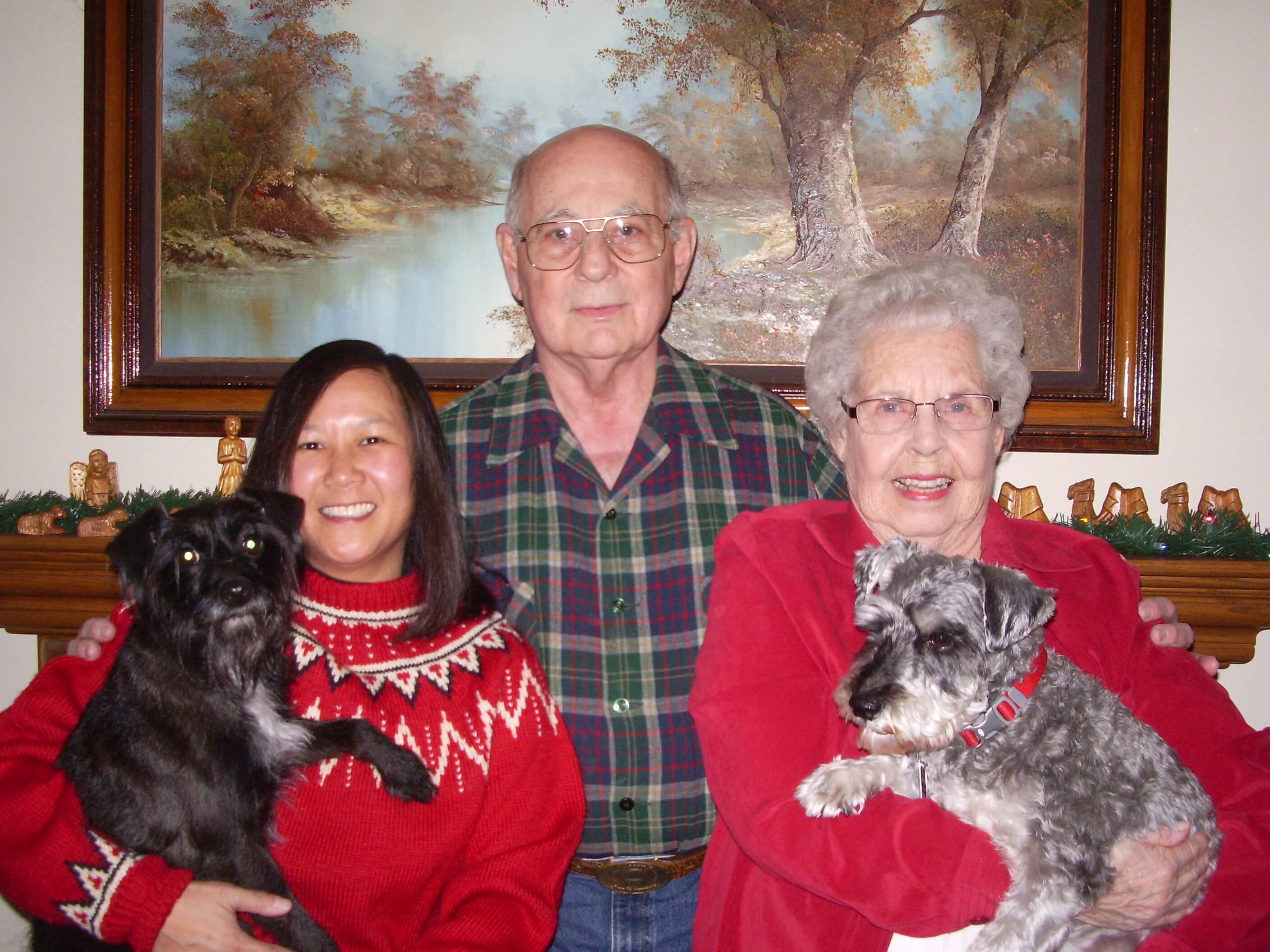 Three adults pose in red holiday sweaters and hold two small dogs.
