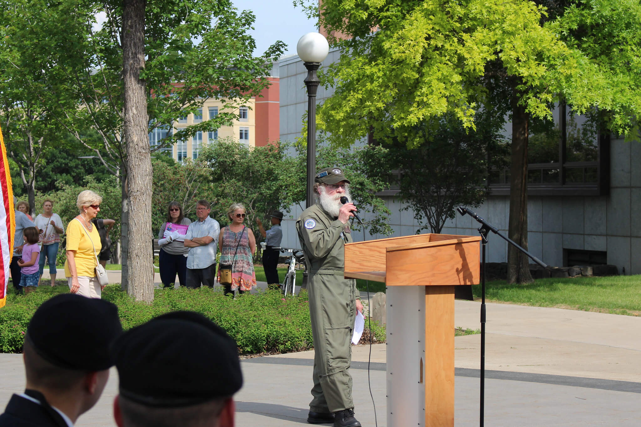 Man in flight suit talks into a microphone at a public outdoor event.