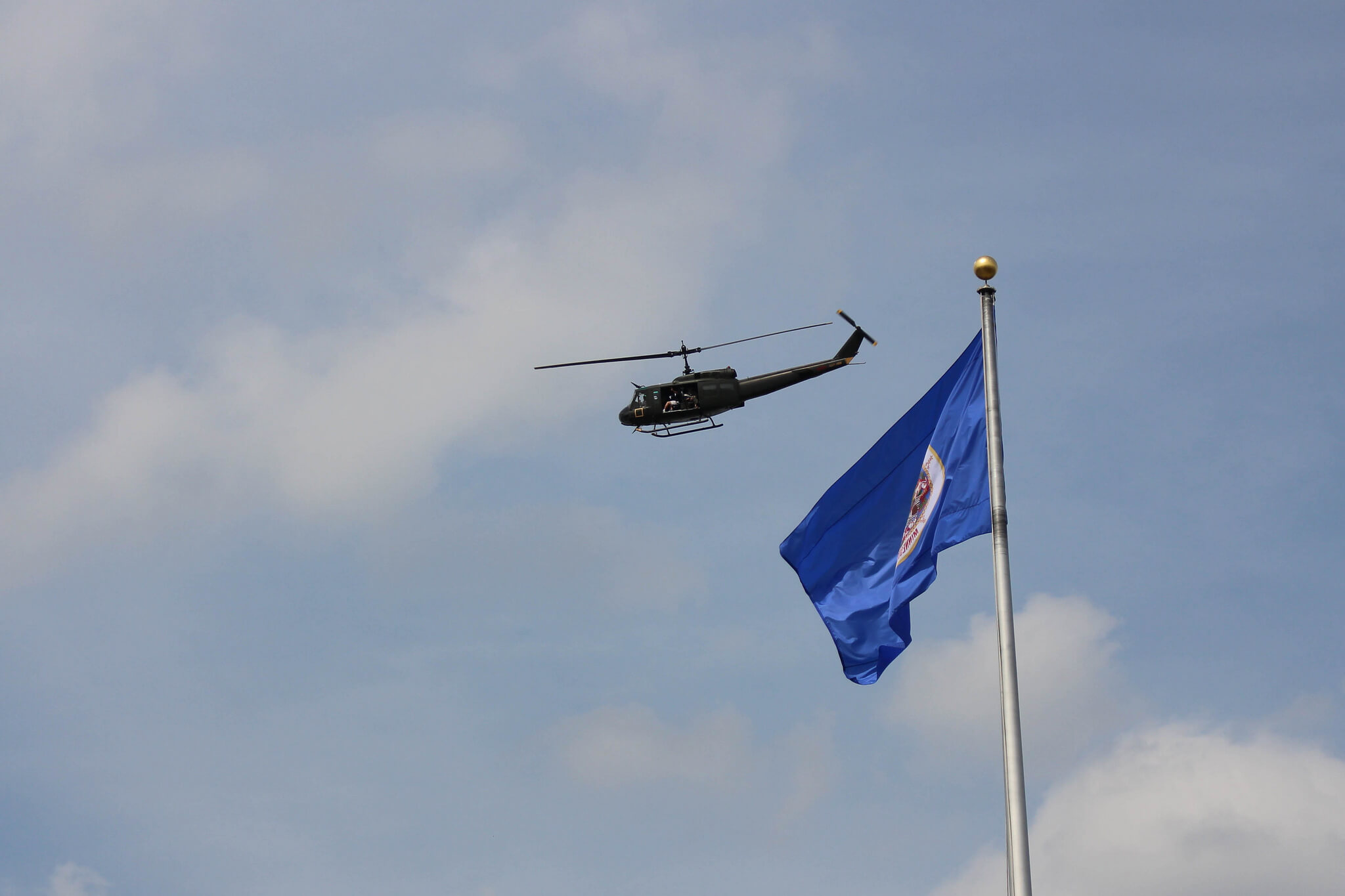 Huey Helicopter hovers over a blue flag at the Minnesota State Capitol.
