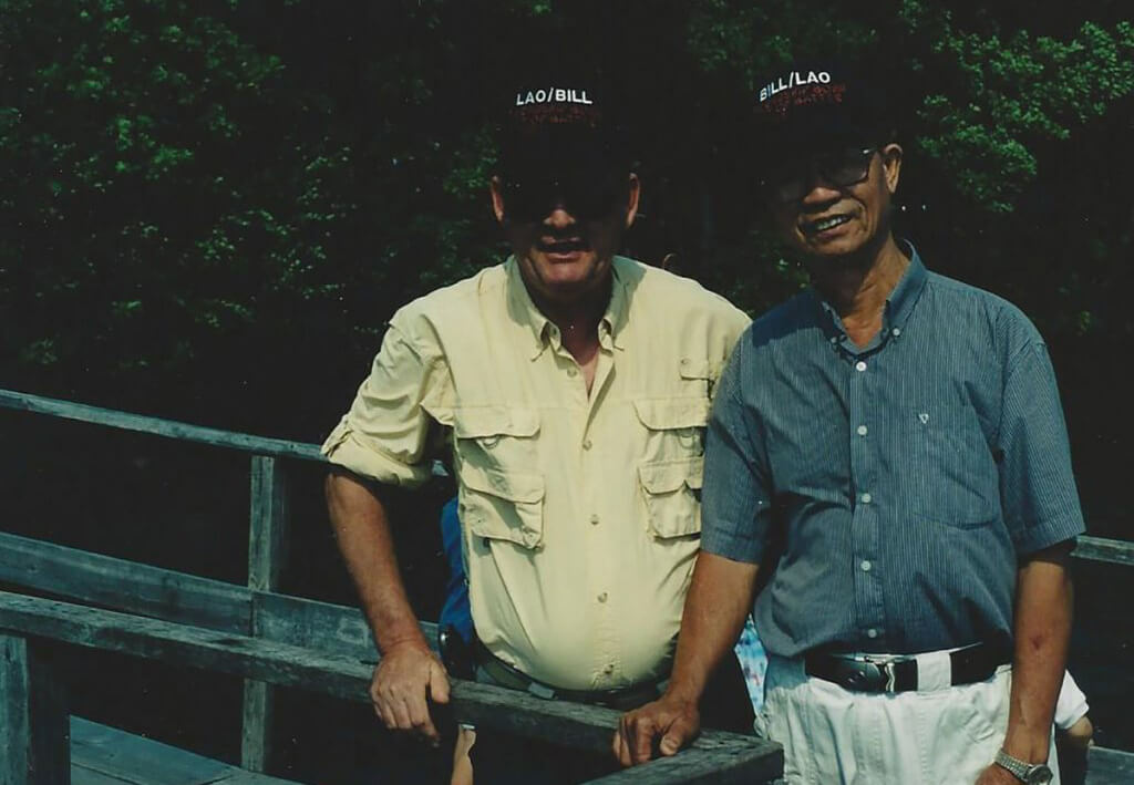 Two men in matching hats that say Bill/Lao.