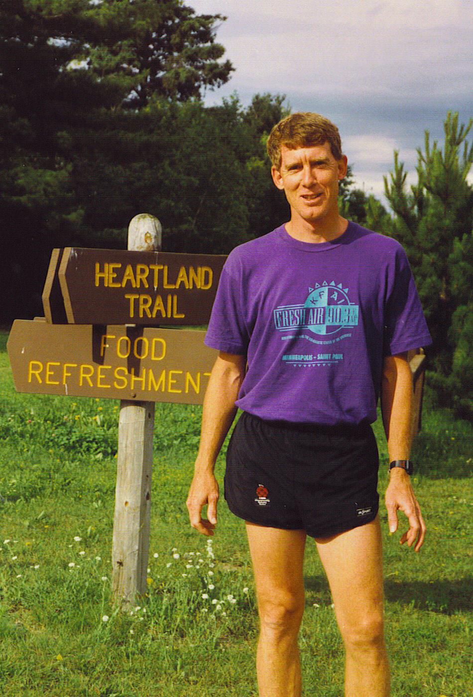 Man in running gear by a trail sign