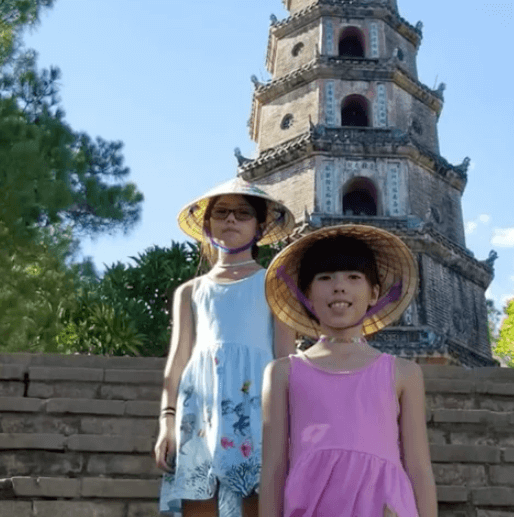 Two girls in conical straw hats in front of a pagoda