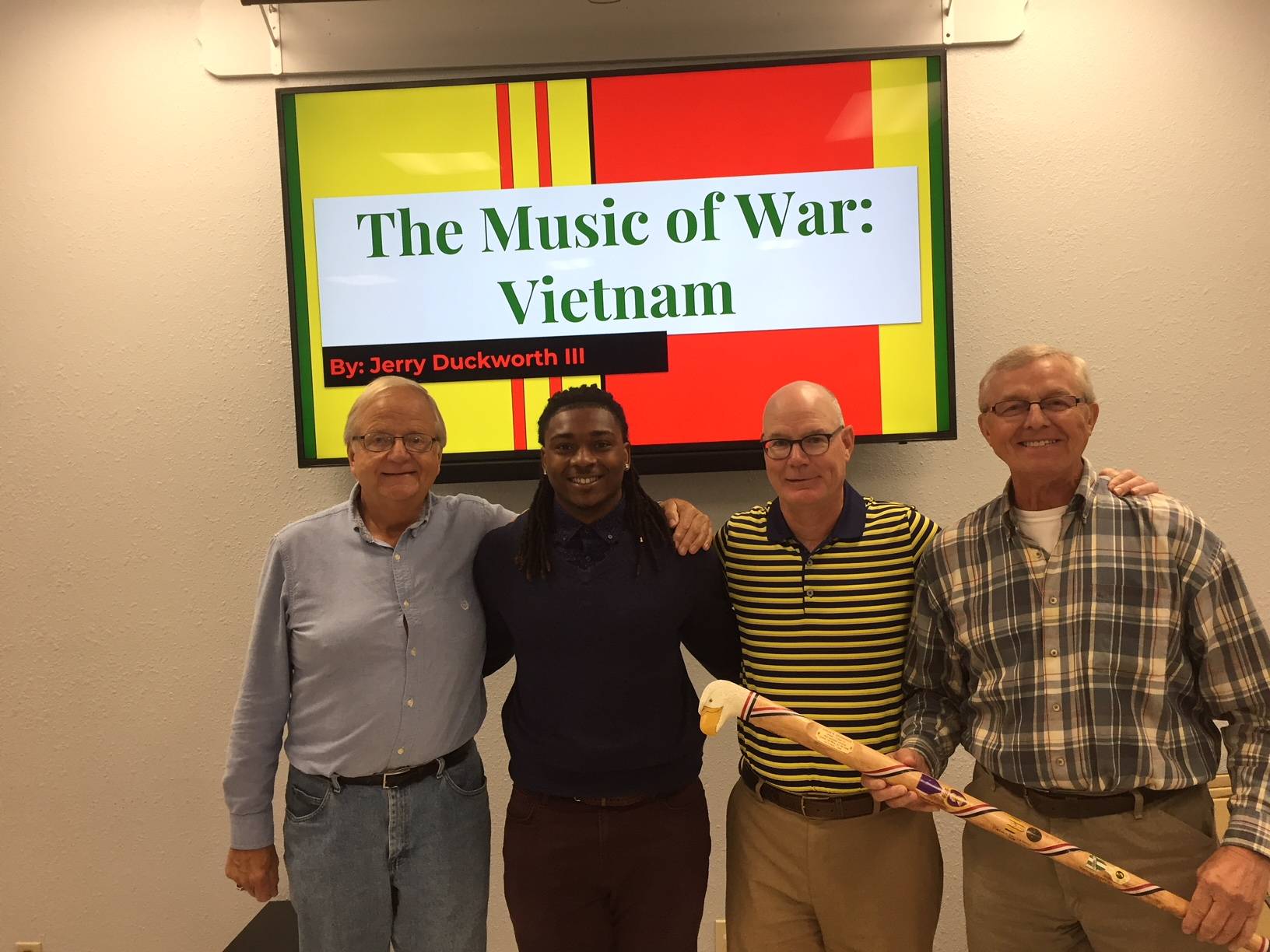 Photo of four men in front of a screen with the text The Music of War: Vietnam